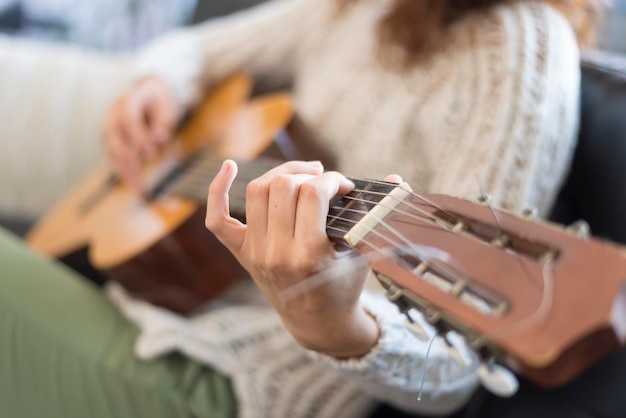 Środkowa sekcja kobiety grającej na gitarze siedzącej w domu