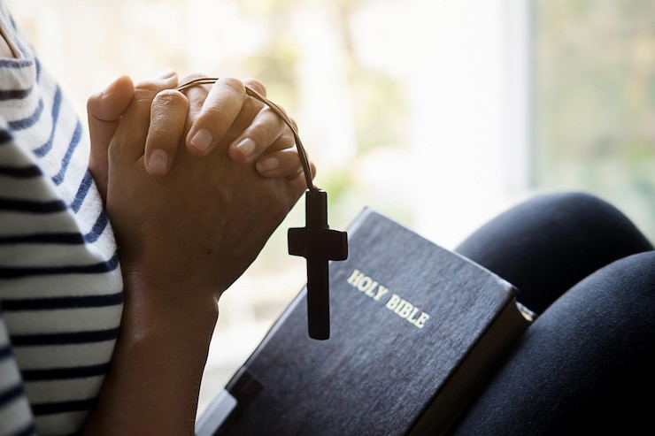 Zdjęcie środkowa sekcja kobiety z krzyżowym wisiorkiem i biblią w domu
