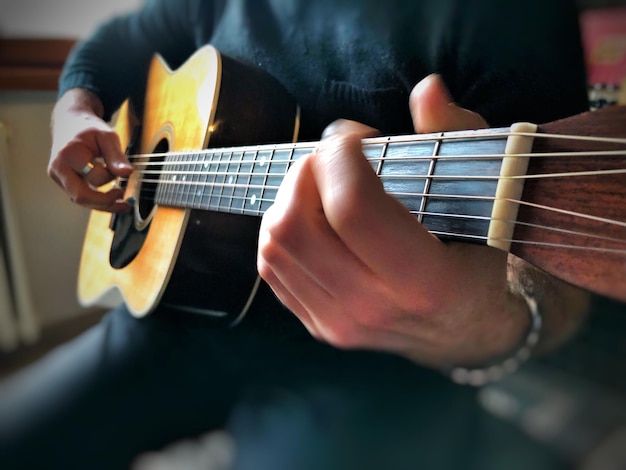 Środkowa sekcja mężczyzny grającego na gitarze siedzącego w domu