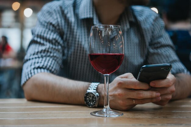 Środkowa sekcja mężczyzny używającego telefonu komórkowego przy kieliszku wina przy stole