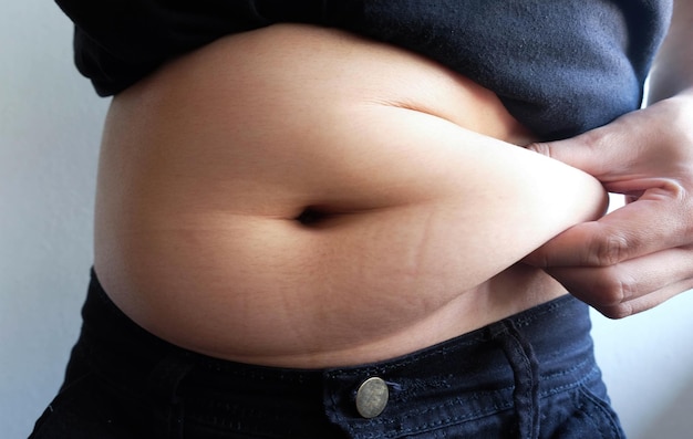 Środkowa Sekcja Nadwagi Kobiety Trzymającej Tłuszcze Brzucha, Stojąc Przy ścianie
