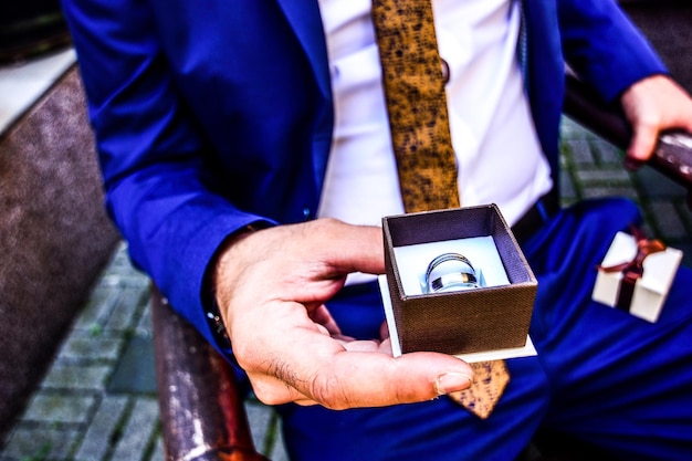 Zdjęcie Środkowa sekcja pana młodego trzymającego pierścienie ślubne siedząc na zewnątrz