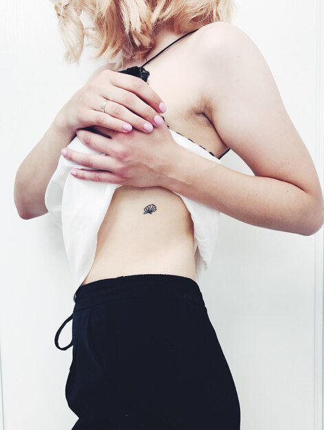 Zdjęcie Środkowy odcinek kobiety z tatuażem na brzuchu na białym tle