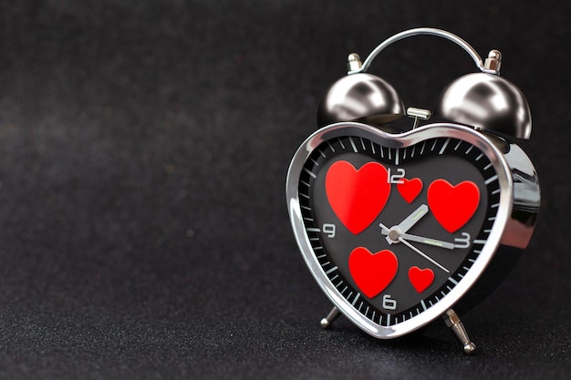 Zdjęcie stalowy budzik w formie serca z czerwonymi sercami w środku na czarnym błyszczącym błyszczącym tle szczęśliwych walentynek