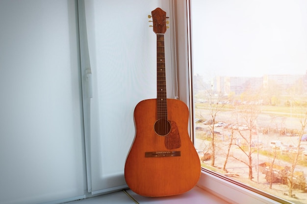 Stara drewniana gitara klasyczna stojąca przy oknie w słoneczny dzień Instrument muzyczny