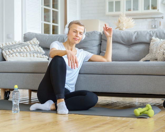 Stara kobieta relaksuje się po zajęciach fitness w domu, słuchając muzyki