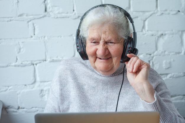 Stara kobieta siedzi przy stole przed laptopem ze słuchawkami.