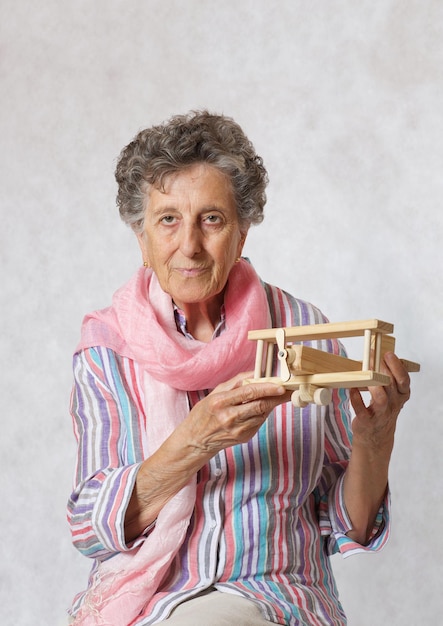 Stara kobieta w wieku od 70 do 80 lat z różowym szalikiem i drewnianym samolotem
