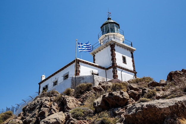 Stara latarnia morska z flagą Grecji na tle błękitnego nieba
