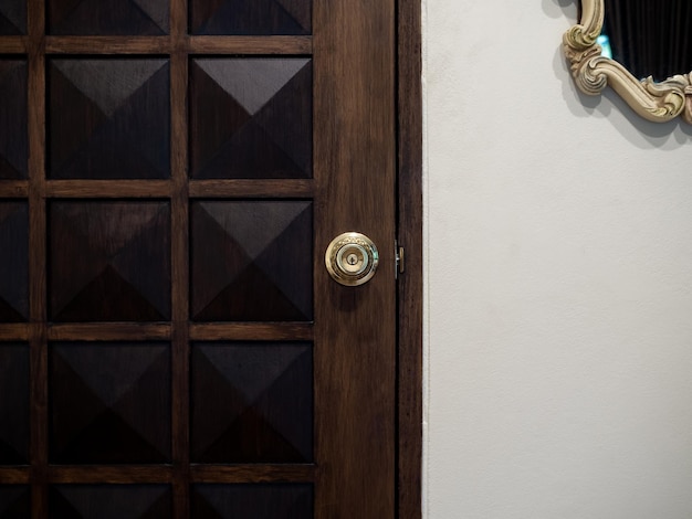 Stara luksusowa mosiężna klamka na drewnianych drzwiach w stylu vintage z lustrem vintage wiszącym na tle białej ściany w białym pokoju
