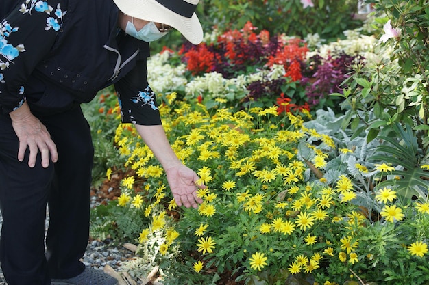 stara starsza kobieta nosząca maskę na twarz relaksująca się w ogrodzie kwiatowym