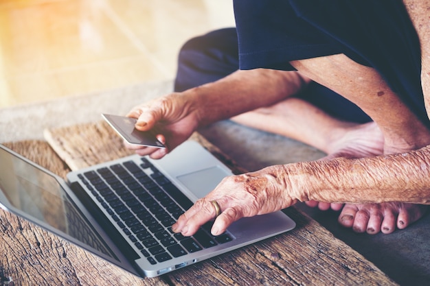 Stara starsza kobieta używa laptop i rękę trzyma kredytowej karty zakupy internet