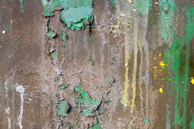 Stara zardzewiała metalowa powierzchnia pokryta kilkoma warstwami łuszczącej się brązowej i zielonej farby z pozostałościami żółtego paintballa