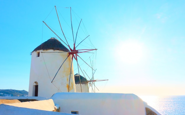 stare białe wiatraki na wyspie mykonos na tle bezchmurnego jasnoniebieskiego nieba ze świecącym słońcem, grecja