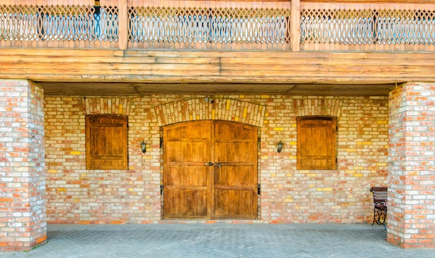 Stare drewniane drzwi w ścianie z cegły. Brama z oknami w ścianie domu.