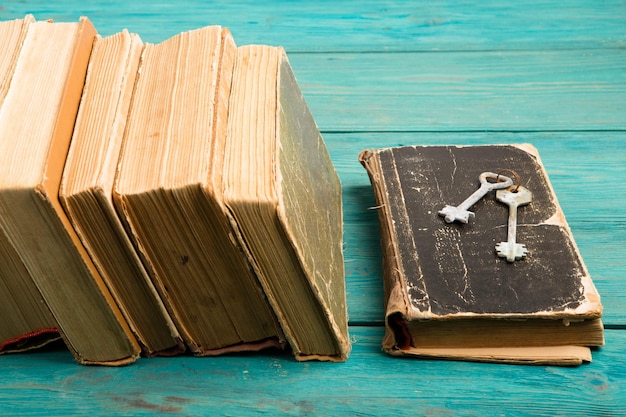 Stare klucze na starej książce i stos antycznych książek na niebieskim drewnianym biurku