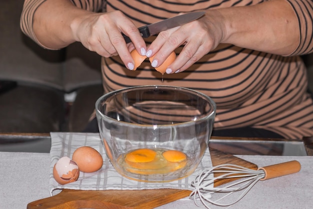 Zdjęcie stare kobiety łamią jajka w szklaną miskę nożem, przygotowując się do zrobienia omletu lub naleśników