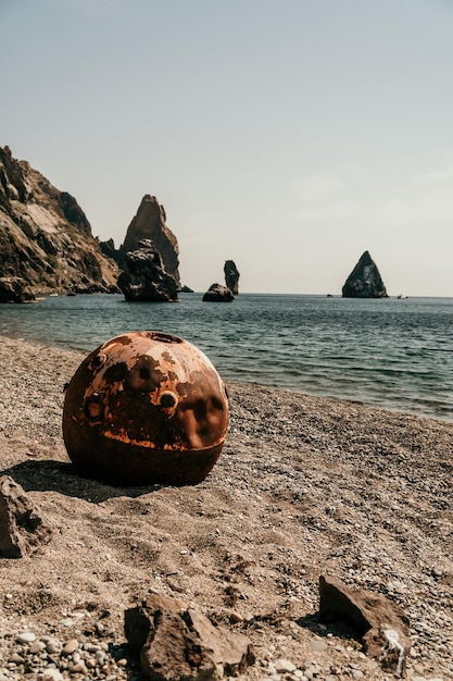 Stare zardzewiałe okrągłe pływające kopalnie morskie na plaży ze skalistym brzegiem i zanieczyszczeniem tła morza