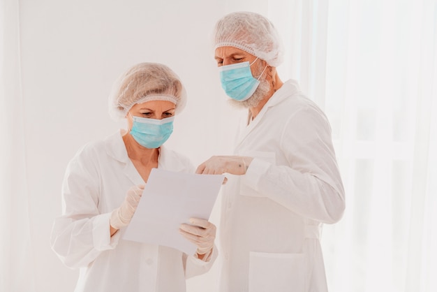 Starsi lekarze z maską na twarz pracują razem w szpitalu
