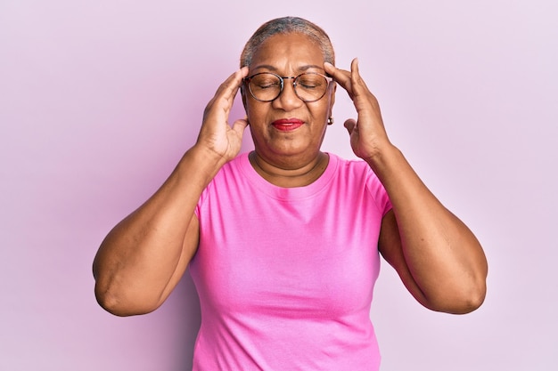Starsza afroamerykanka ubrana w zwykłe ubrania i okulary cierpiąca na ból głowy zdesperowana i zestresowana z powodu bólu i migreny ręce na głowie