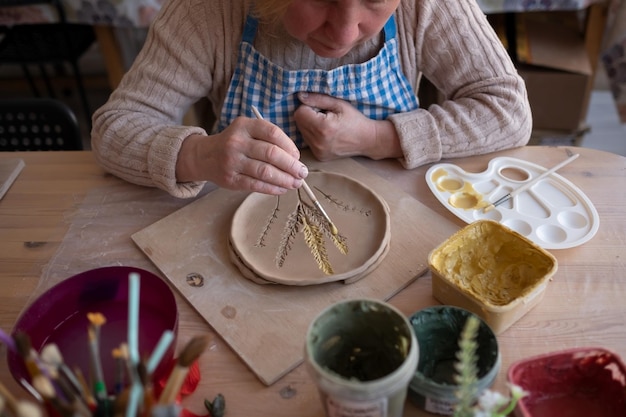 Zdjęcie starsza artystka wykonująca ozdoby kwiatowe na produkcie ceramicznym