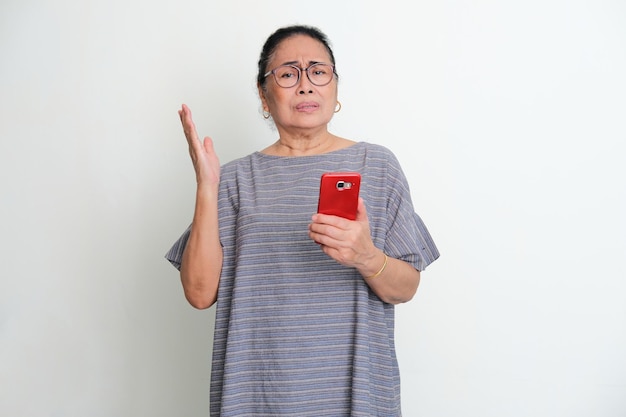 Starsza Azjatka pokazująca zdezorientowany wyraz twarzy, gdy trzyma telefon komórkowy