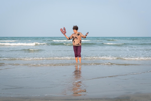 Starsza azjatycka kobieta stojąca na plaży z wodą morską na nogach