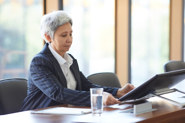Starsza bizneswoman siedzi przy stole i przy użyciu komputera podczas seminarium w sali konferencyjnej