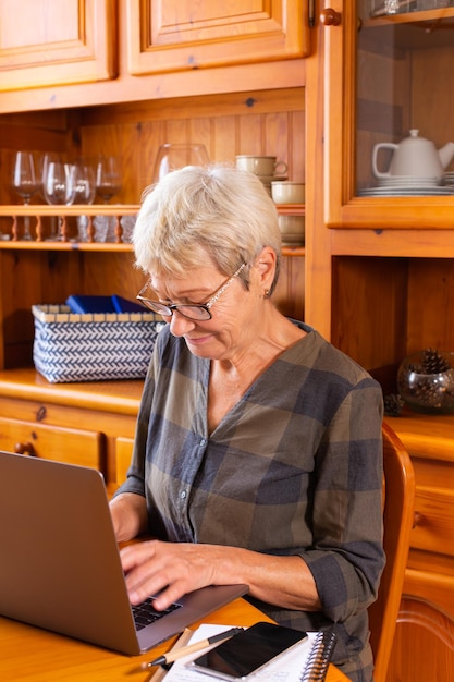 Starsza dojrzała kobieta korzysta z laptopa w domu oglądając webinarium online