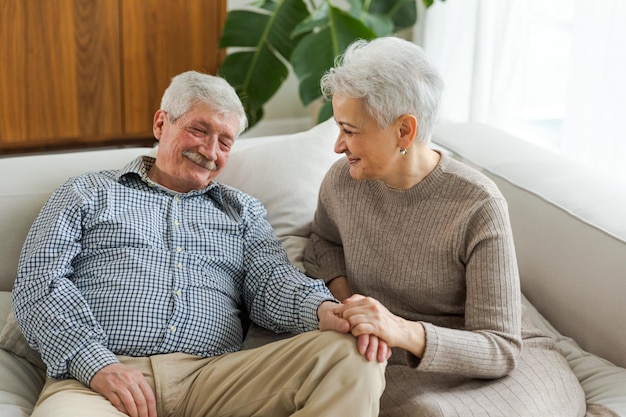 Zdjęcie starsza dorosła para zakochana trzymająca się za ręce w domu w średnim wieku stary mąż i żona patrzą z t