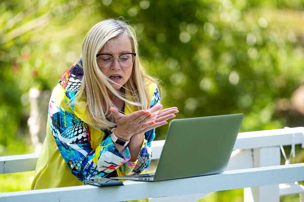 Zdjęcie starsza emocjonalna kobieta z laptopem wykonującą rozmowę wideo i aktywnie gestującą komunikację internetową