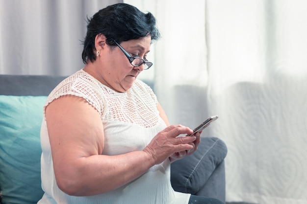 Starsza kobieta 60-letnia latynoska babcia patrząca na swój telefon komórkowy szczęśliwa w domu w domu