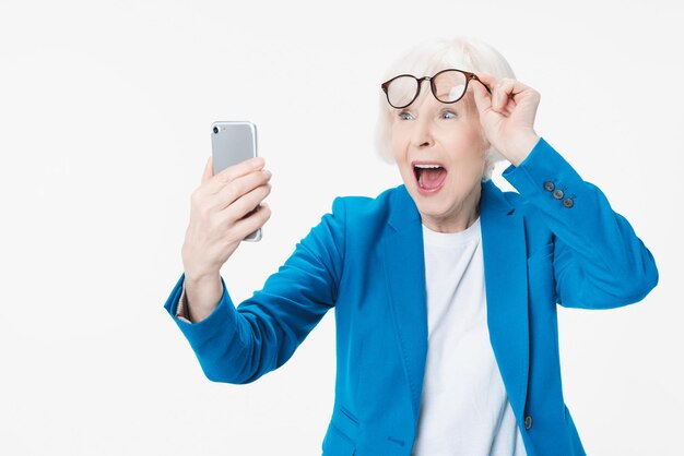 Starsza kobieta bardzo szczęśliwa i podekscytowana, używająca smartfona na białym tle