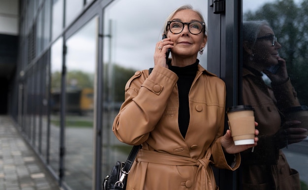 Starsza kobieta biznesu idzie do pracy rozmawiając przez telefon komórkowy lidera w koncepcji biznesowej