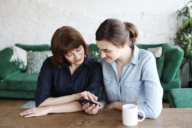 Starsza kobieta i jej dorosła córka korzystają ze smartfona w domu