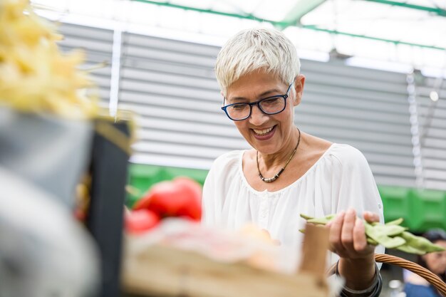 Starsza kobieta kupuje świeżego organicznie warzywa na rynku