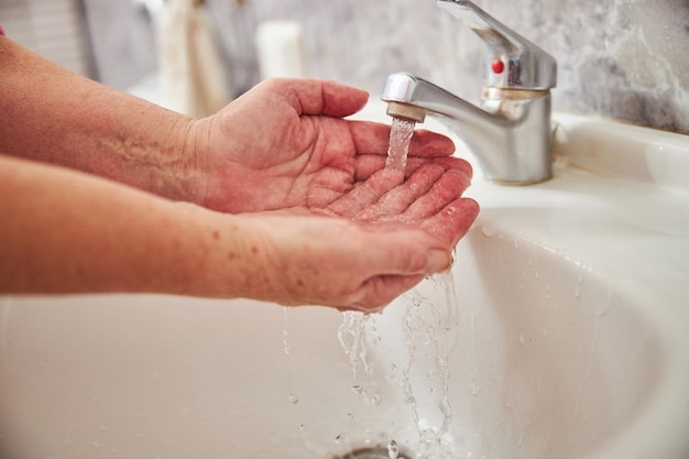 Starsza kobieta myje ręce pod bieżącą wodą