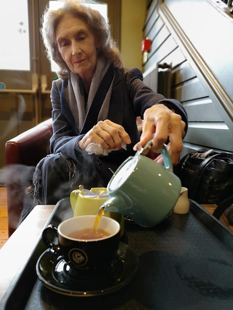 Zdjęcie starsza kobieta nalewa herbatę do filiżanki w domu