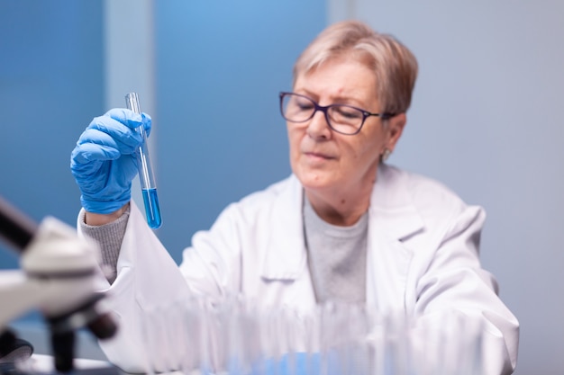 Starsza kobieta naukowiec patrząca na probówkę do testu biochemicznego