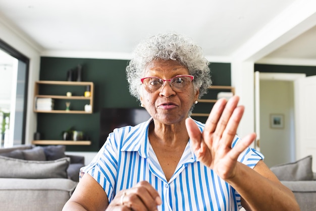 Starsza kobieta o siwych włosach gestuje znakiem stopu ręką podczas rozmowy wideo w domu