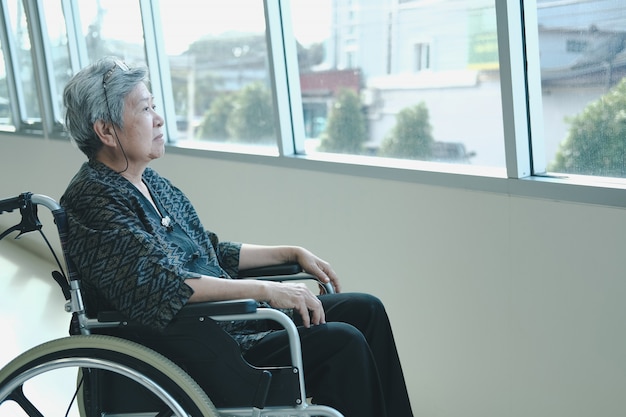 Starsza kobieta odpoczywa blisko okno na wózku inwalidzkim.