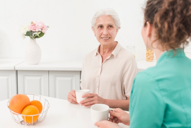 Starsza kobieta patrzeje żeńskiej pielęgniarki podczas gdy pijący kawę