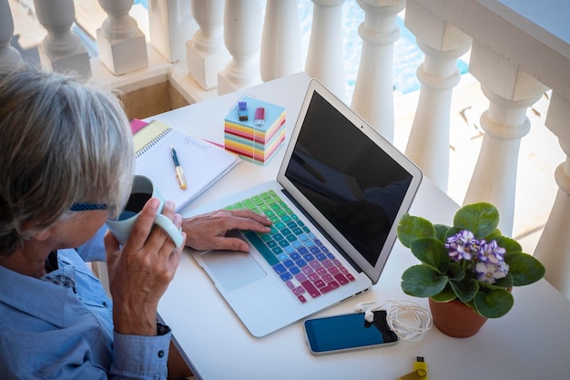 Zdjęcie starsza kobieta pije kawę przy stole za pomocą laptopa