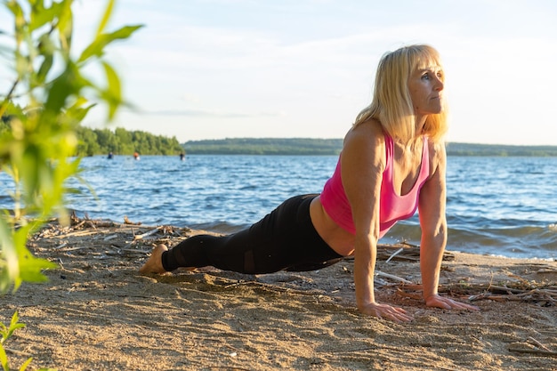 Starsza kobieta podnosząca głowę ćwiczy jogę na brzegu jeziora latem Medytacja Sporty na starość Joga na brzegu Sporty letnie