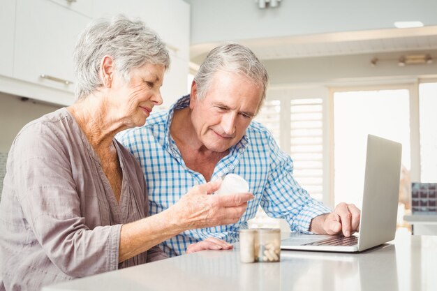 Starsza kobieta pokazuje pigułki mąż z laptopem