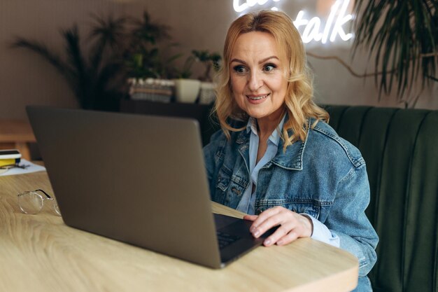 Starsza kobieta siedzi w kawiarni i pracuje na laptopie Dojrzała kobieta w kawiarni korzysta z laptopa