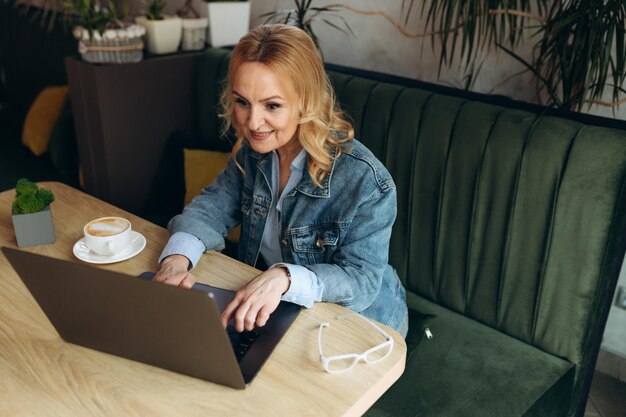 Zdjęcie starsza kobieta siedzi w kawiarni i pracuje na laptopie dojrzała kobieta w kawiarni korzysta z laptopa