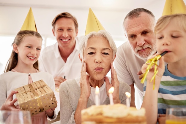 Zdjęcie starsza kobieta świętuje urodziny z rodziną w domu w imprezowych czapeczkach i dmuchając w gwizdki babcia patrzy na tort urodzinowy i jest radosna w otoczeniu męża i syna wnuków