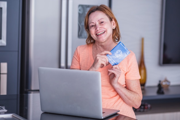 Starsza kobieta trzyma brazylijski karty pracy i komputer. Starsza kobieta trzyma skoroszyt z koncepcją domowego biura.