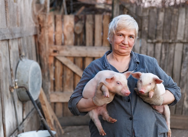 Starsza kobieta trzyma w rękach dwie małe świnki. hodowla zwierząt